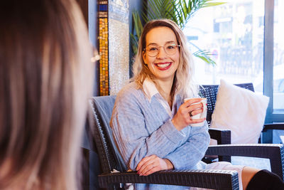 Smiling woman looking at friend while having coffee
