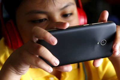 Close-up of boy using phone while listening music against black background