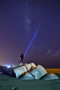 Rear view of man holding illuminated flashlight standing at beach against star field