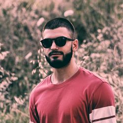 Portrait of young man wearing sunglasses while standing against plants