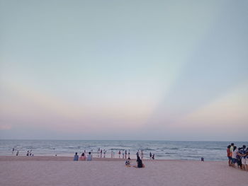 People at beach against clear sky during sunset