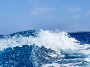 Waves splashing on shore against blue sky