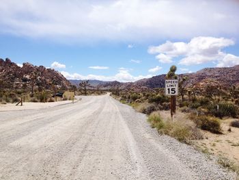 Speed limit sign by road leading towards mountains against sky