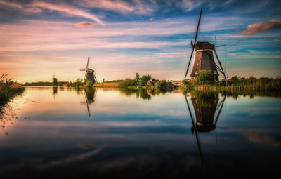 Reflection of traditional windmill in lake against sky during sunset