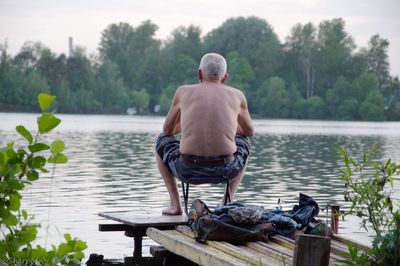 Rear view of senior man sitting on pier by lake