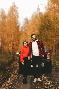 A romantic couple in love in warm sweaters is walking traveling by car in the autumn forest in fall