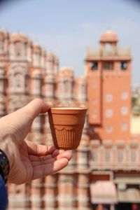 Close-up of hand holding coffee cup against buildings in city