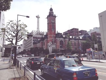 Traffic on road by buildings in city against sky