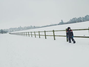 Man walking on snow covered railing against clear sky