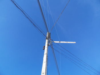 Low angle view of electricity pylon against clear blue sky