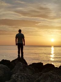 Rear view of silhouette man standing on beach against sky during sunset