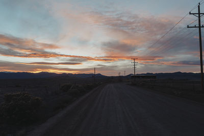 Road amidst field against sky during sunset