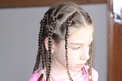 Close-up of girl with braided hair looking away against wall