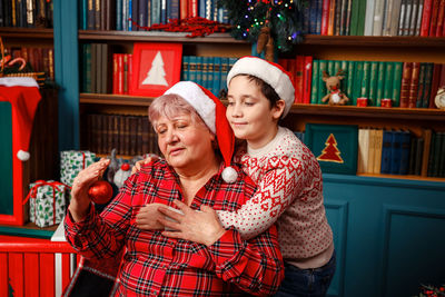 Little son and grandmother decorating christmas tree together at home.