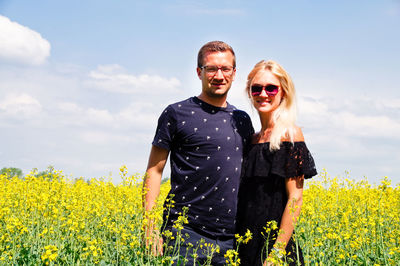 Portrait of couple standing amidst yellow flowers on oilseed rape field