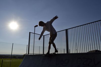 Full length of teenage boy skateboarding against clear sky at park