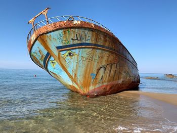 Damaged boat on beach against clear sky