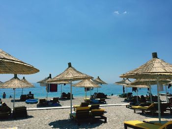 Parasols and lounge chairs at beach against blue sky on sunny day