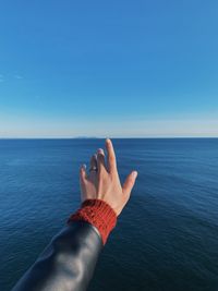 Close-up of hand gesturing against sea against clear blue sky