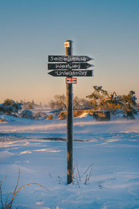 Information sign on snow covered land against sky during sunset
