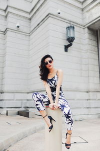 Full length of woman sitting on bollard against building