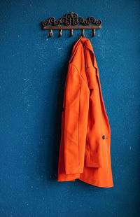 Metal hooks on the background of a blue wall. a red women's jacket is hanging on a hanger.