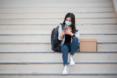 Woman using mobile phone by box on staircase