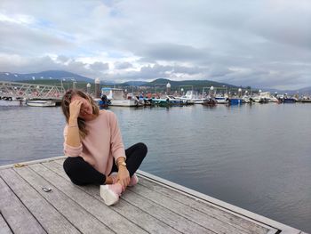 Woman sitting on pier over sea against sky