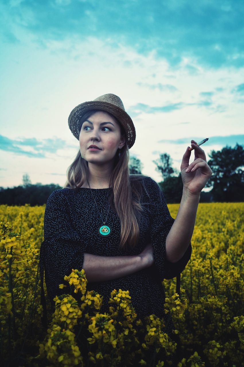 one person, real people, plant, young adult, clothing, leisure activity, lifestyles, hat, standing, nature, waist up, front view, women, young women, land, sky, portrait, field, beauty in nature, beautiful woman, hair, hairstyle, outdoors