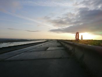 Empty footpath by beach against sky during sunset