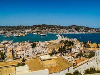 High angle view of townscape by sea against clear blue sky