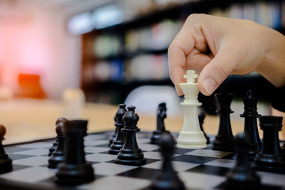 Cropped hand of woman playing chess on table in library