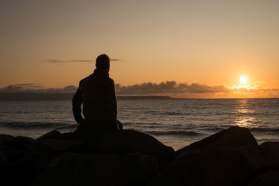 Silhouette man looking at sea against sky during sunset