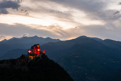 Scenic view of illuminated church on mountain range against sky during sunset