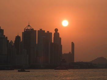 Silhouette buildings by sea against sky during sunset