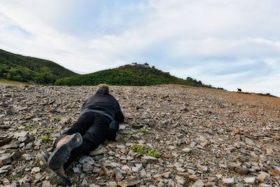 Man on rock on field against sky