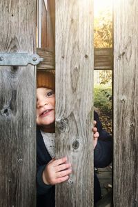 Portrait of smiling boy peeking through wooden fence