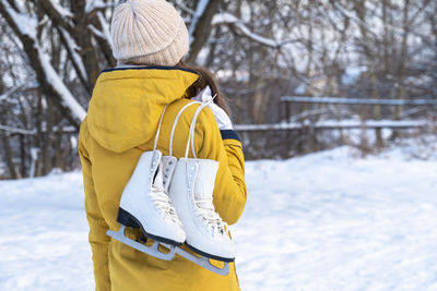 Young woman in yellow jacket with ice skates walking through snowy park