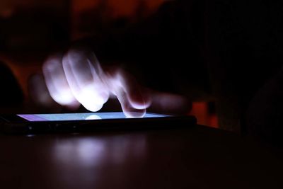 Close-up of hand using mobile phone in darkroom