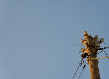 Low angle view of telephone pole against clear blue sky