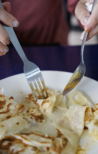 Woman cutting a plate of roti canai flatbread with fork and spoon