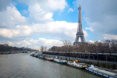 Low angle view of eiffel tower by river against cloudy sky on sunny day