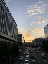 Traffic on road amidst buildings against sky during sunset