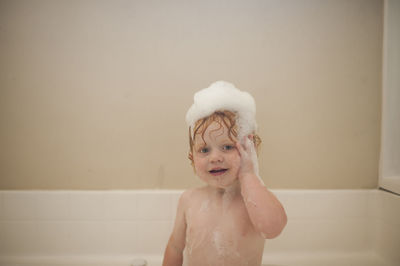 Portrait of cute baby boy bathing in bathtub at home