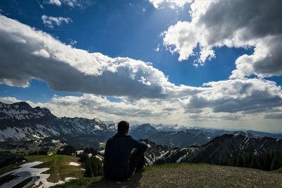 Rear view of man sitting on mountain against sky