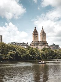 Buildings by river against cloudy sky