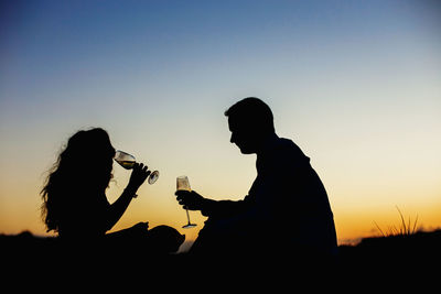 Silhouette couple having drinks against clear sky during sunset