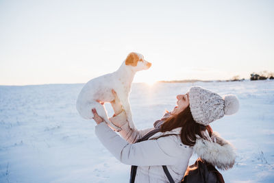 Side view of woman holding dog while standing outdoors during winter
