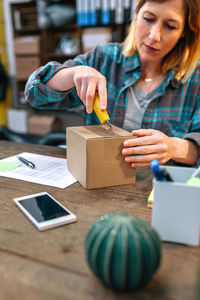 Young female entrepreneur with cutter opening wrong package sent to client in online shop