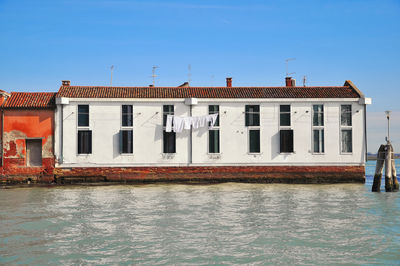 Buildings by river against clear blue sky